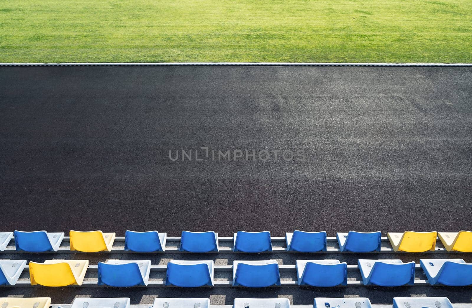 top view of tribune row empty plastic seats in blue and yellow near an outdoor stadium arena with green grass on playing field in front