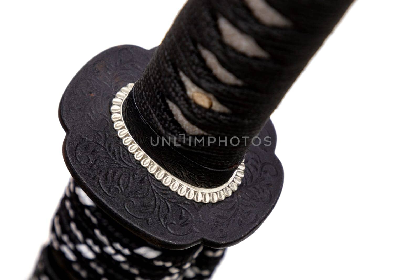 Close up shot of Tsuba - hand guard of Japanese sword made by steel isolated in white background. The sword handle wrapped by black silk cord and white ray skin. Selective focus.