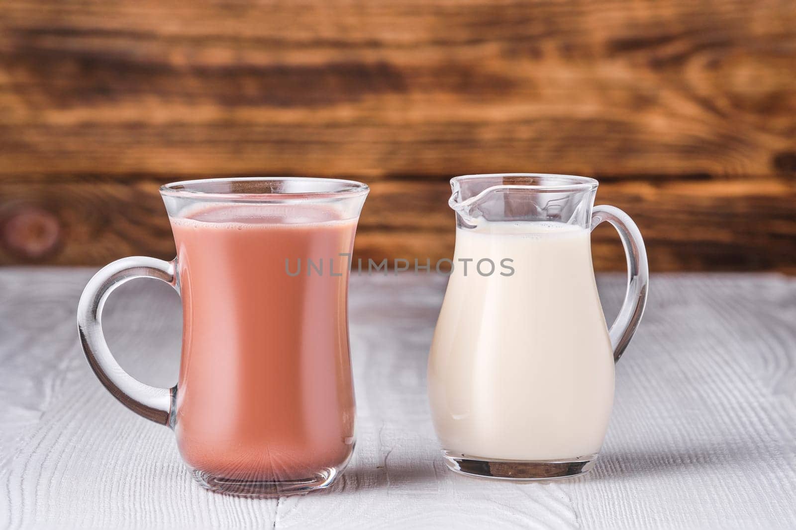 Chocolate milk and soy milk in glass on white table over dark wooden background