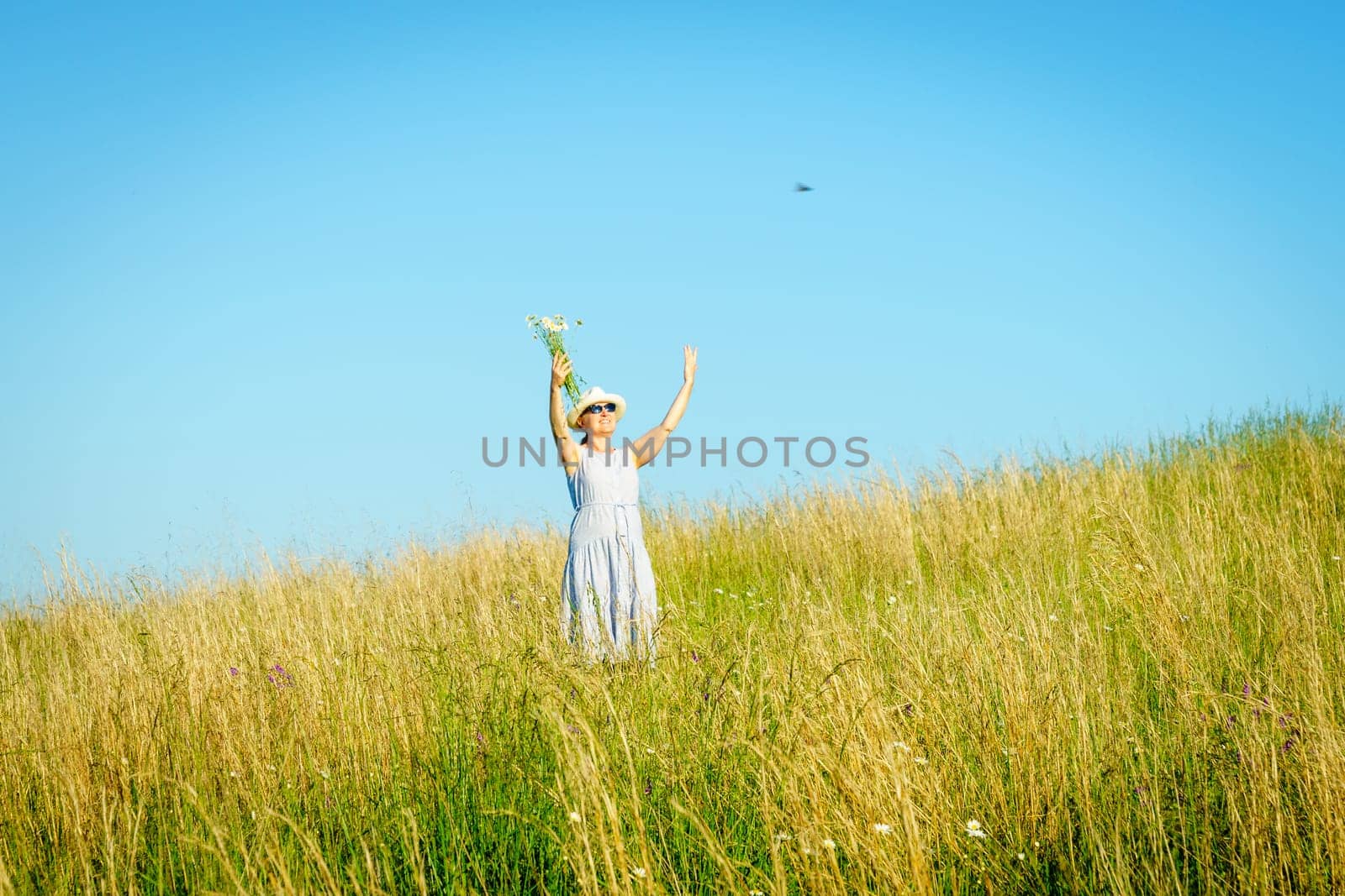 Happy mature woman with wildflowers in a tall grass field on a bright summer day.