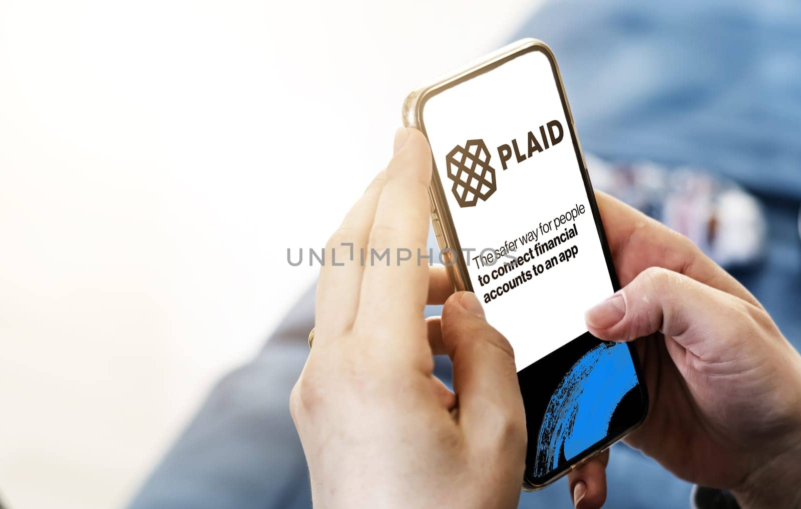 San Francisco, USA, June 2022: Female hands holding a phone with Plaid homepage on screen. Plaid logo blurred on a blue background. Plaid is a financial services company based in San Francisco