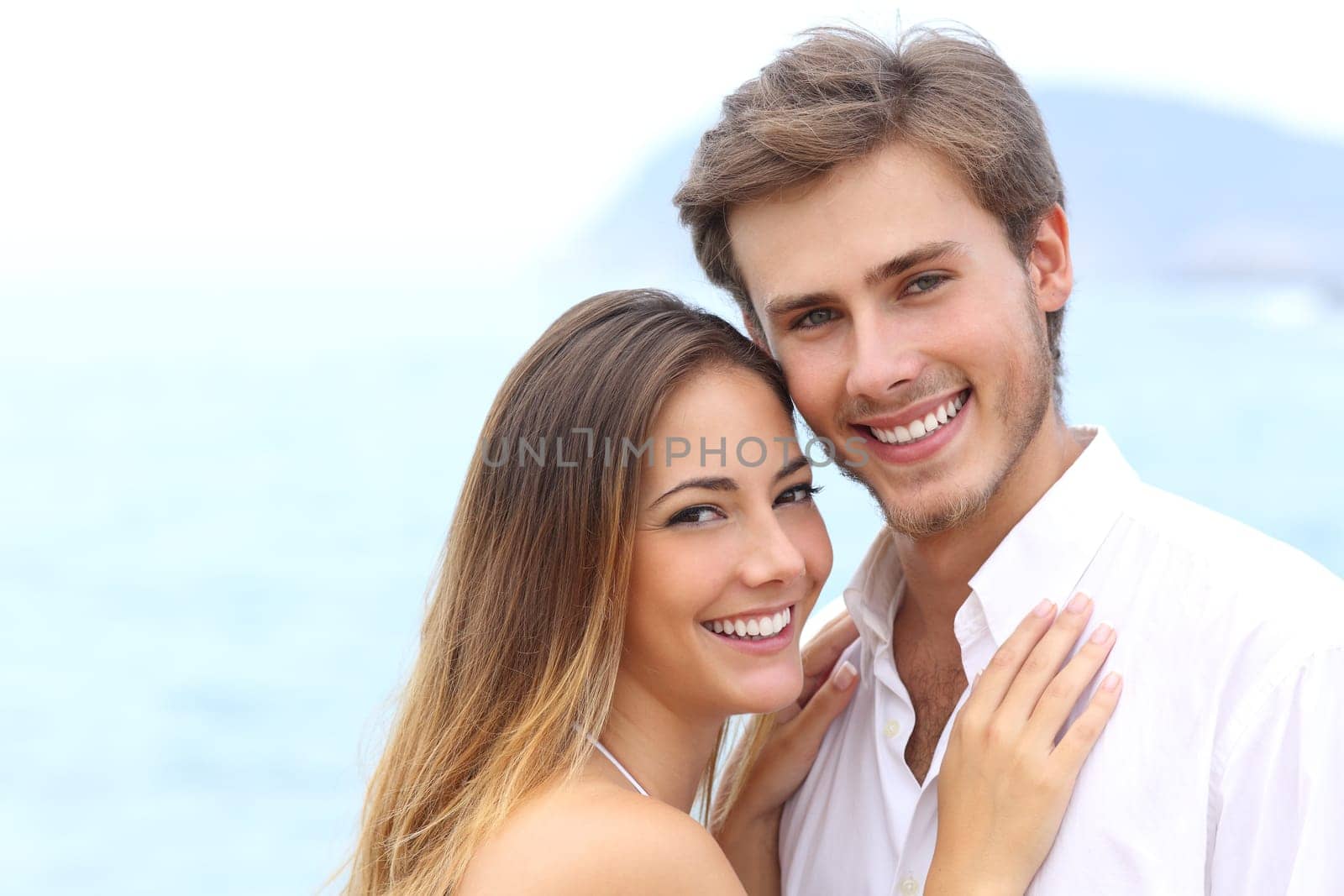 Happy couple with a white smile looking at camera on holidays on the beach isolated on white above