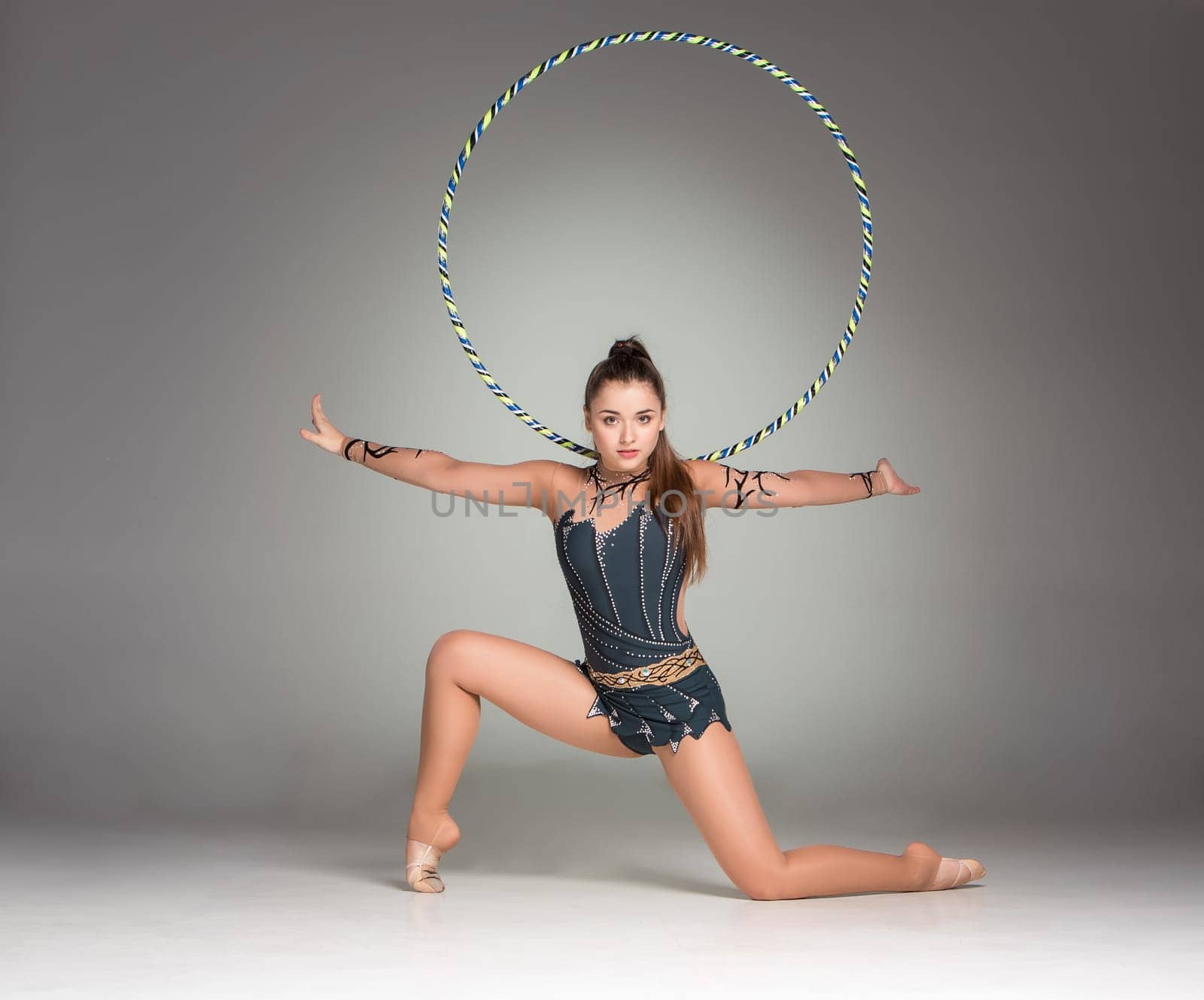 teenager doing gymnastics exercises with colorful hoop on a gray background
