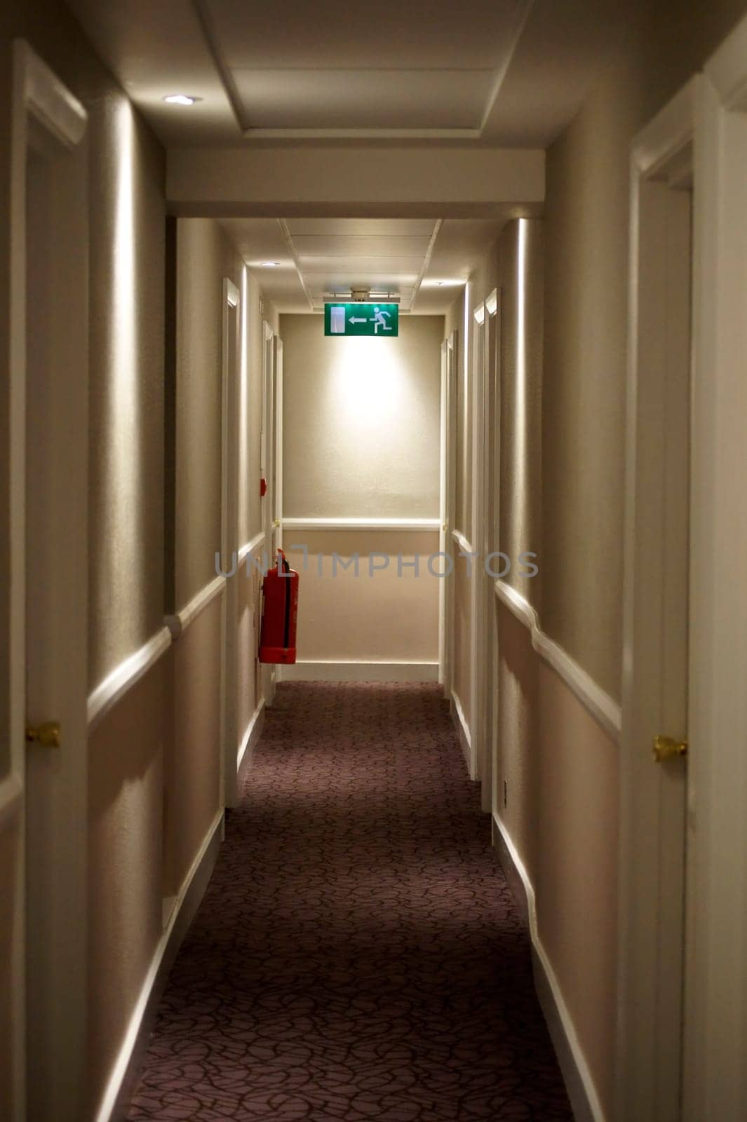 A narrow hallway with a fire extinguisher and an emergency exit.