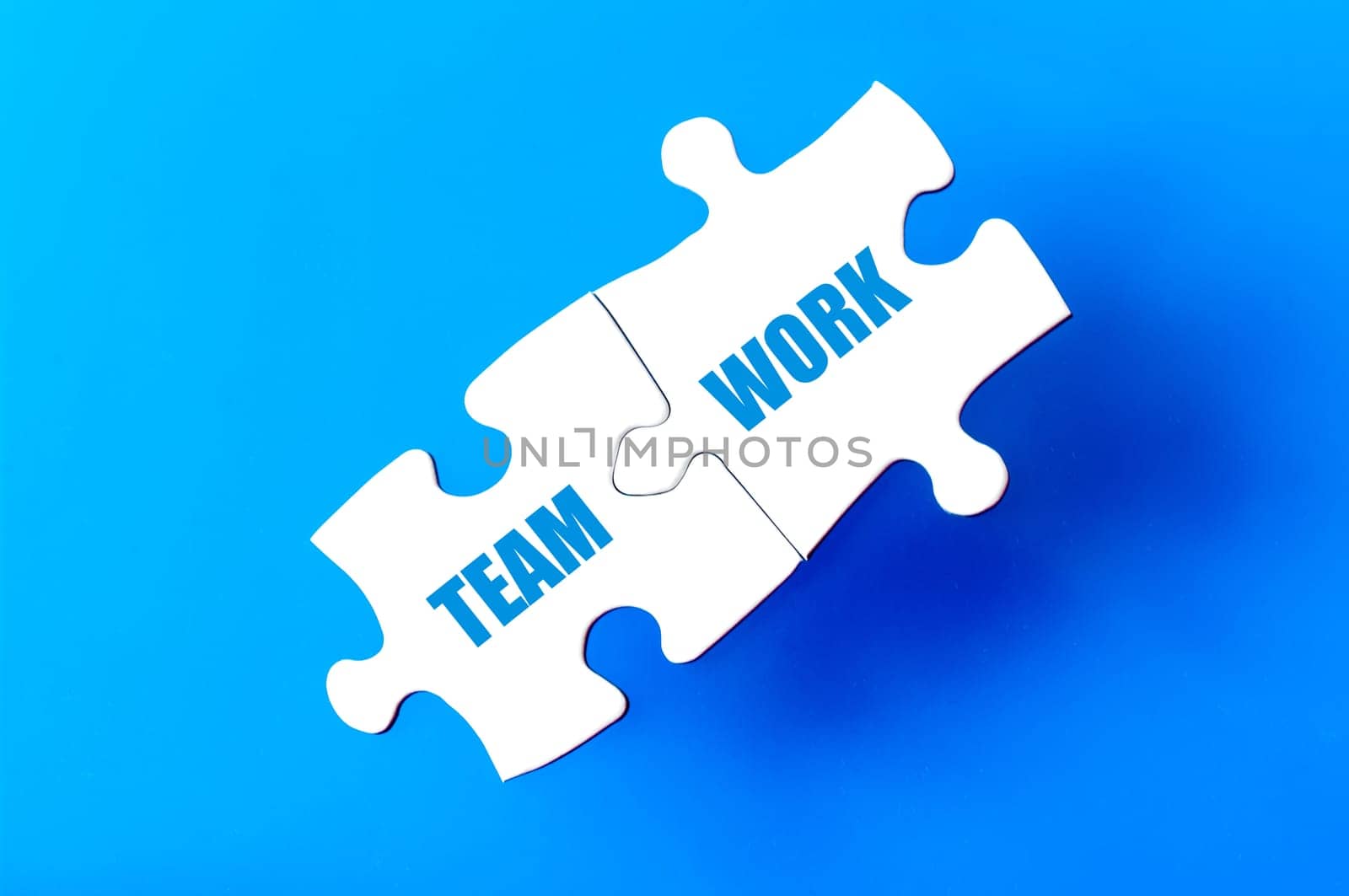 Connected puzzle pieces with words TEAM and WORK  isolated over blue background, with copy space available. Business concept image.
