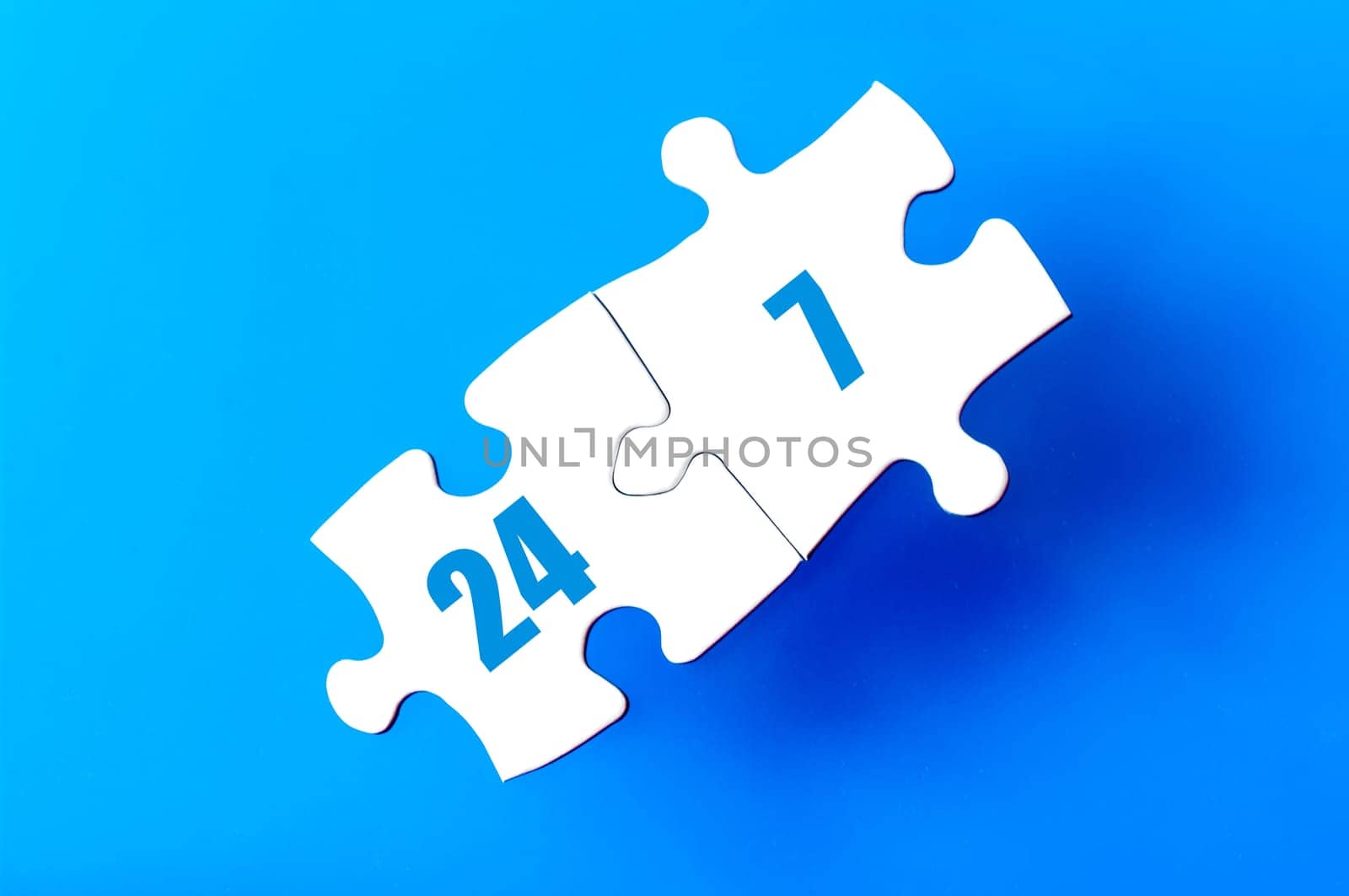 Connected puzzle pieces with text twenty four seven  isolated over blue background, with copy space available. Business concept image.