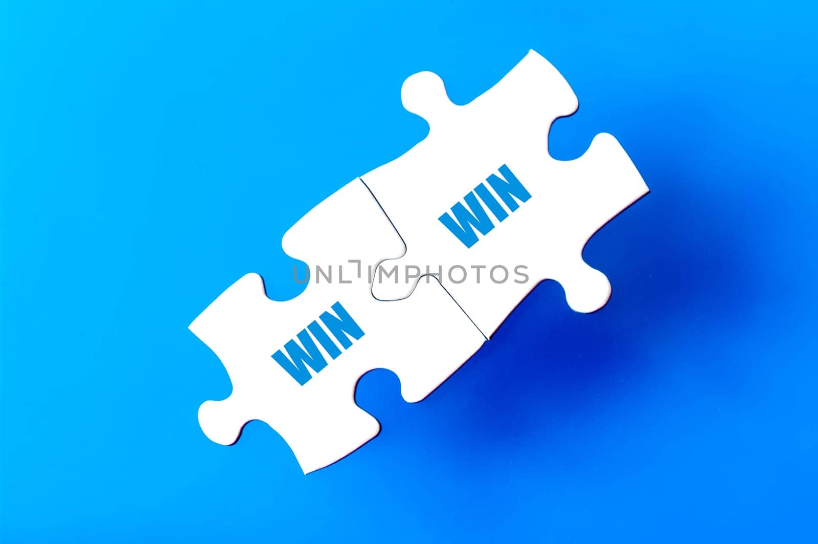 Connected puzzle pieces with words WIN and WIN  isolated over blue background, with copy space available. Business concept image.