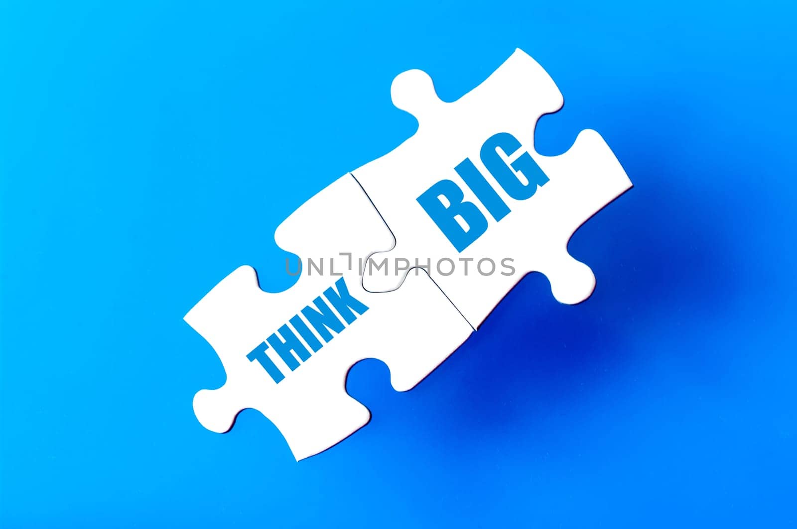 Connected puzzle pieces with text THINK BIG  isolated over blue background, with copy space available. Business concept image.