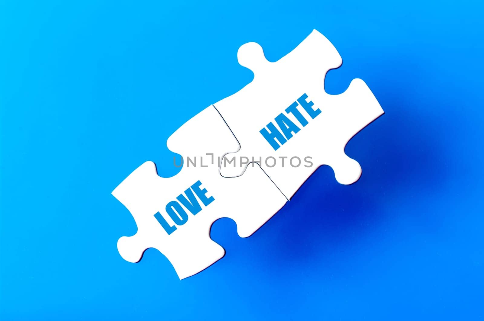 Connected puzzle pieces with words LOVE and HATE  isolated over blue background, with copy space available. Business concept image.