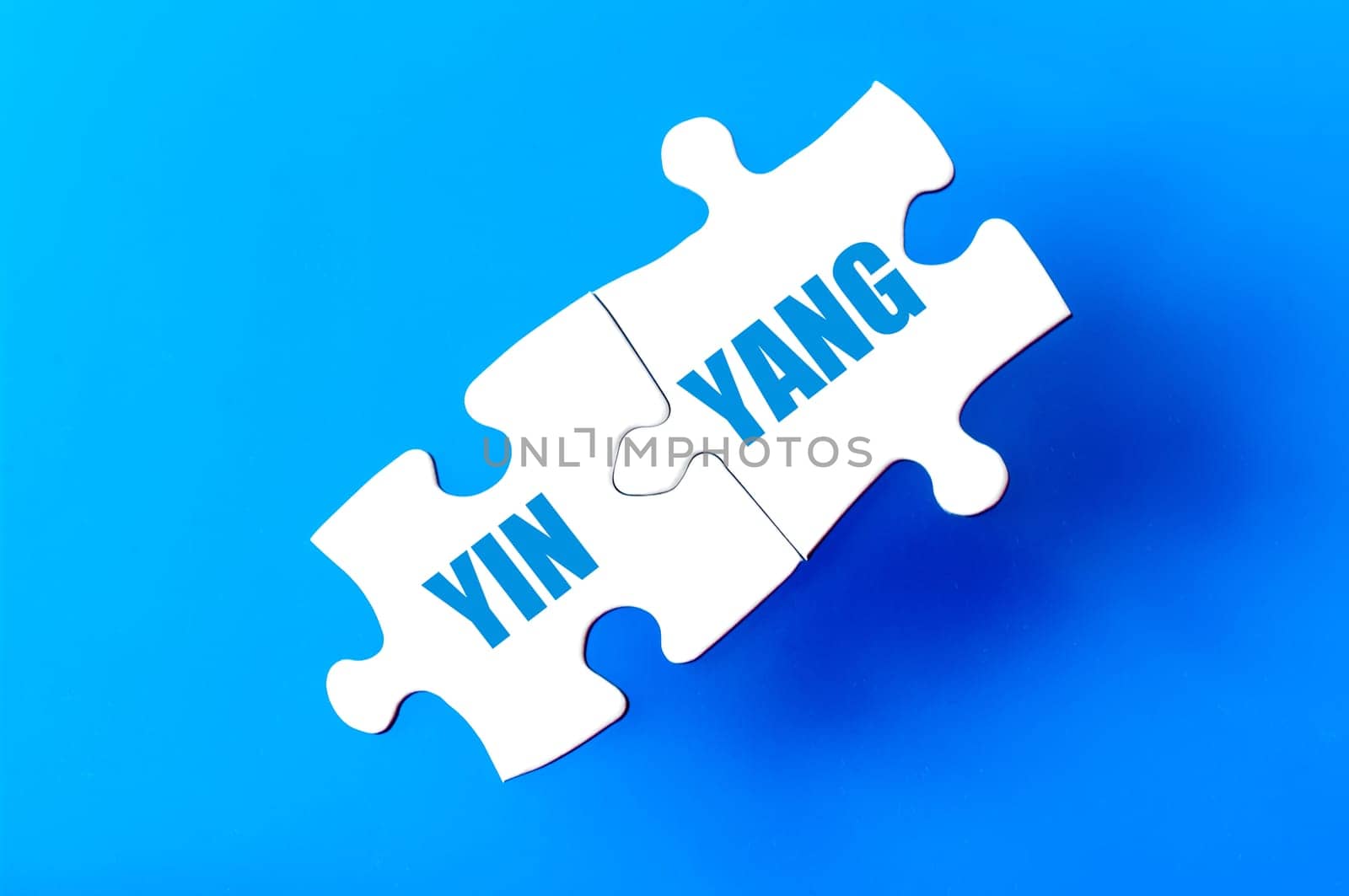Connected puzzle pieces with words YIN YANG isolated over blue background, with copy space available. Business concept image.
