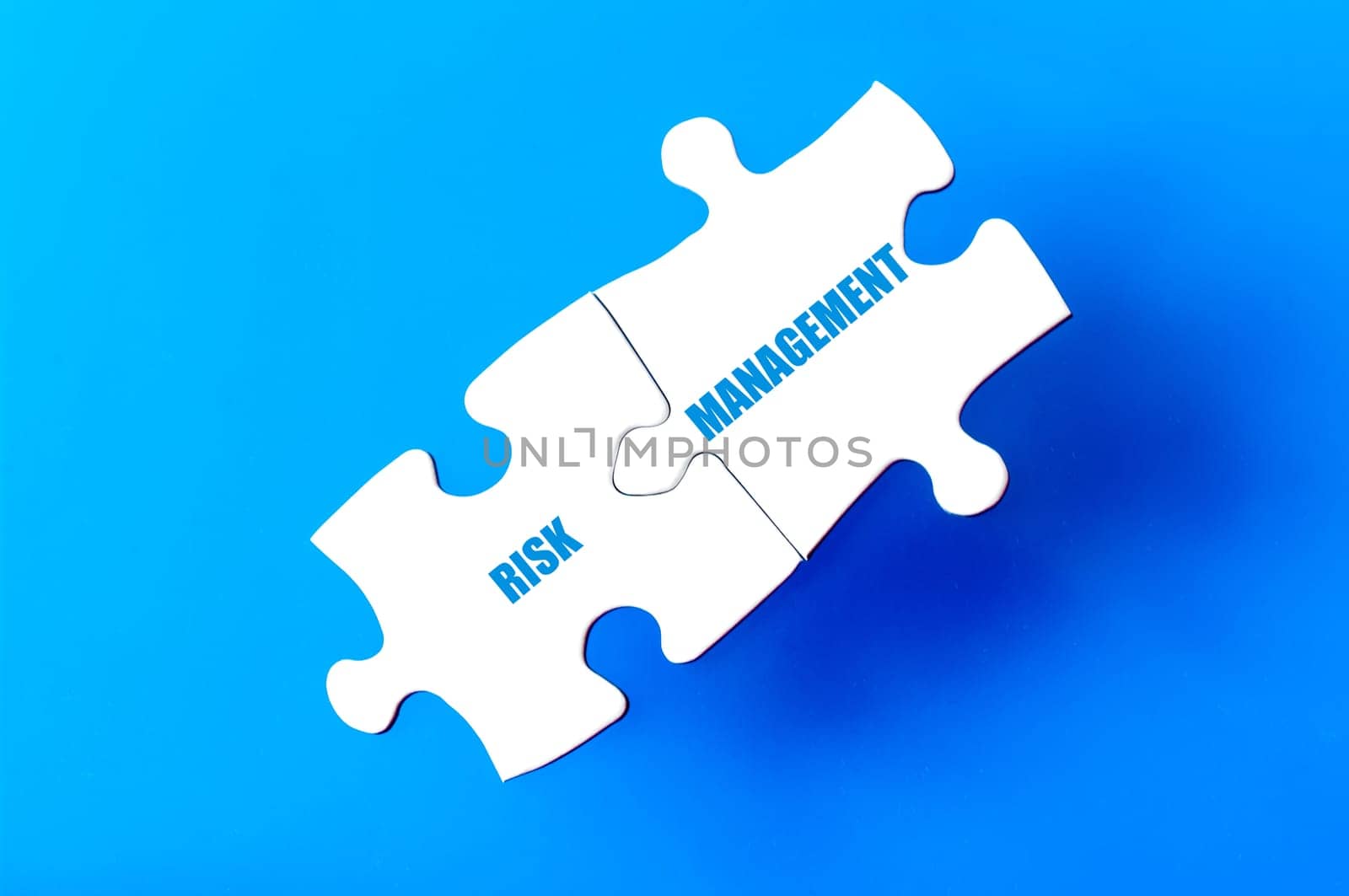 Connected puzzle pieces with words RISK and MANAGEMENT  isolated over blue background, with copy space available. Business concept image.