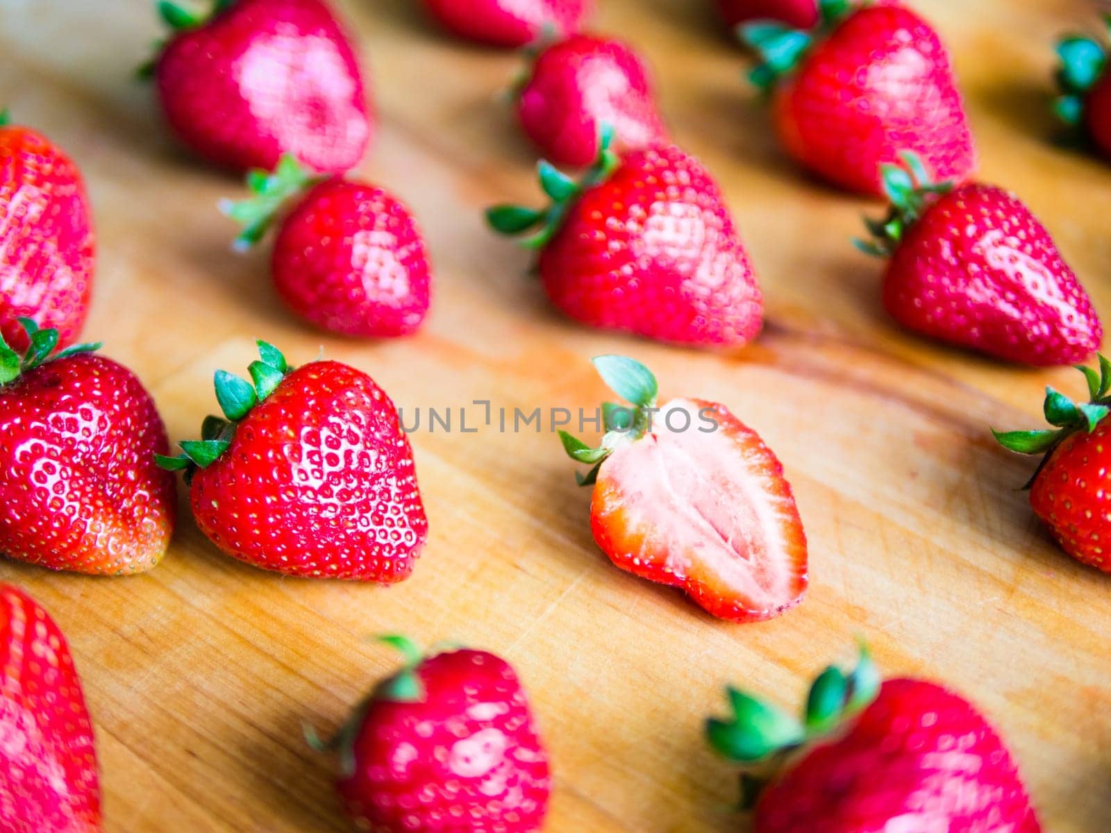 One cutted strawberry in an srranged pattern of strawberries on a wooden board, difference expression
