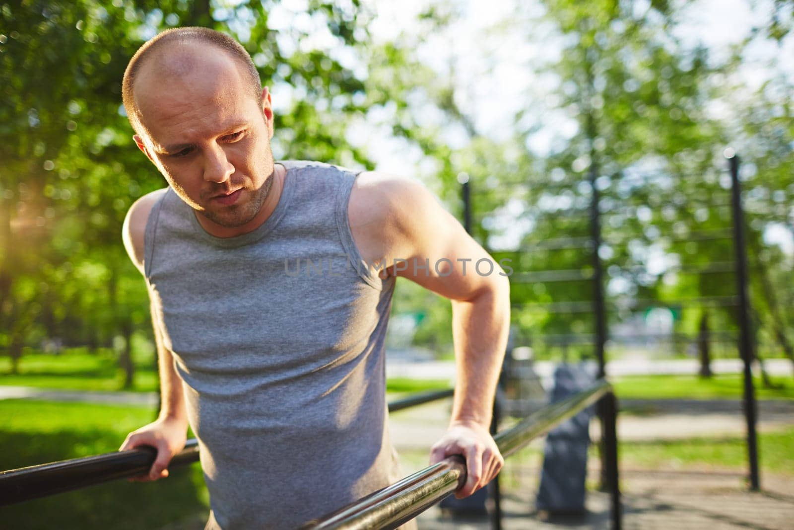 Young man in grey vest training on sport equipment outside