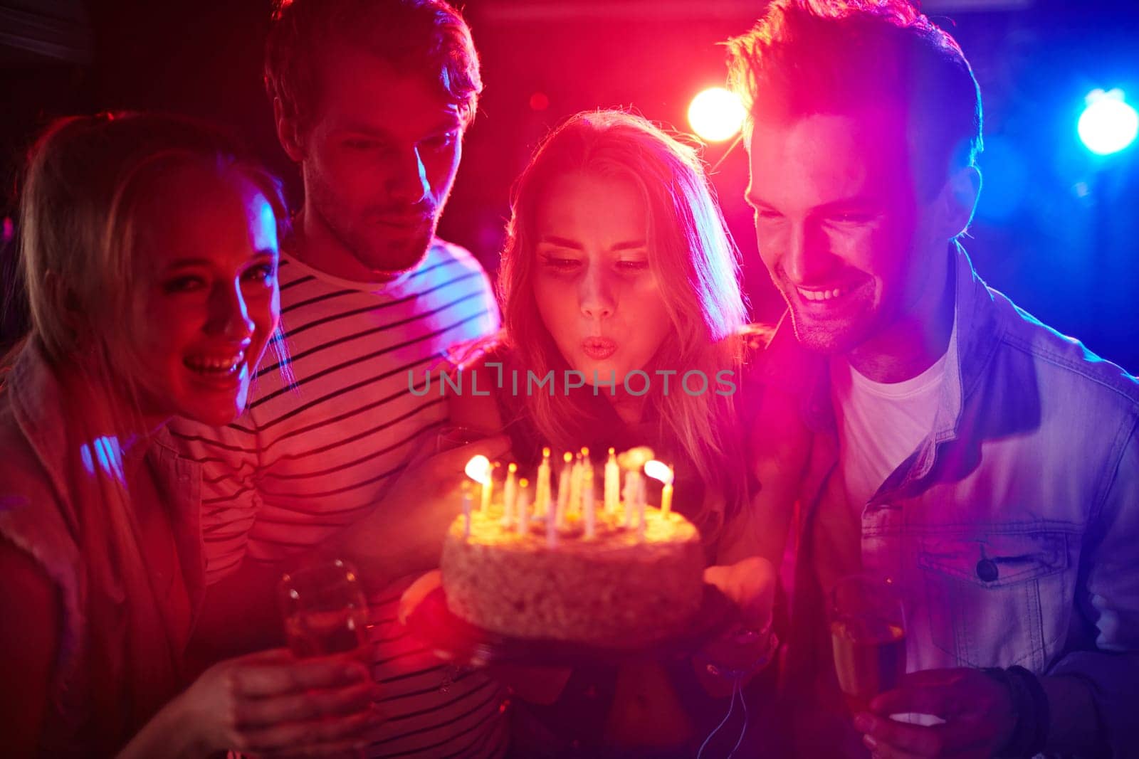 Young girl blowing candles on birthday cake between her friends