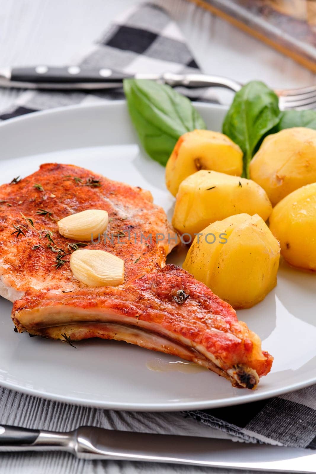 Steak with bone and potato baked in oven in a roasting pan with garlic and thyme