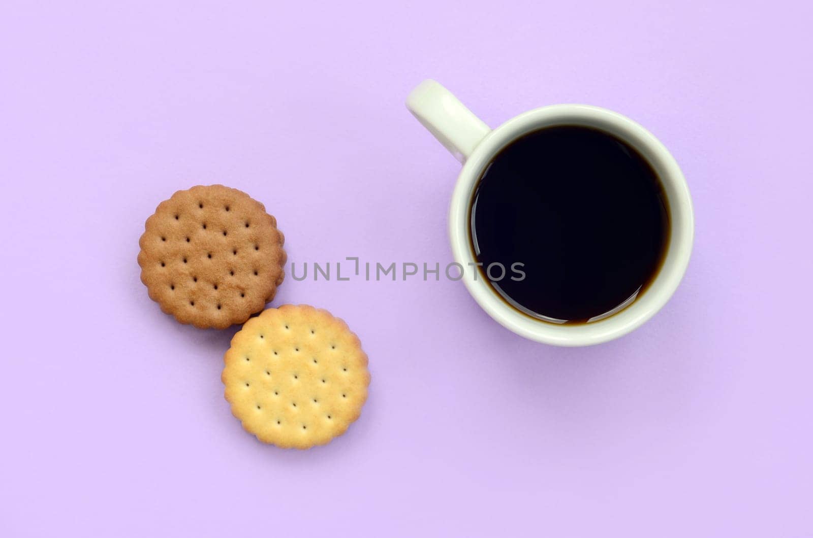 Coffee break flat lay composition with brown sandwich cookies. White hot coffee cup and brown dessert on a trendy pastel lilac background