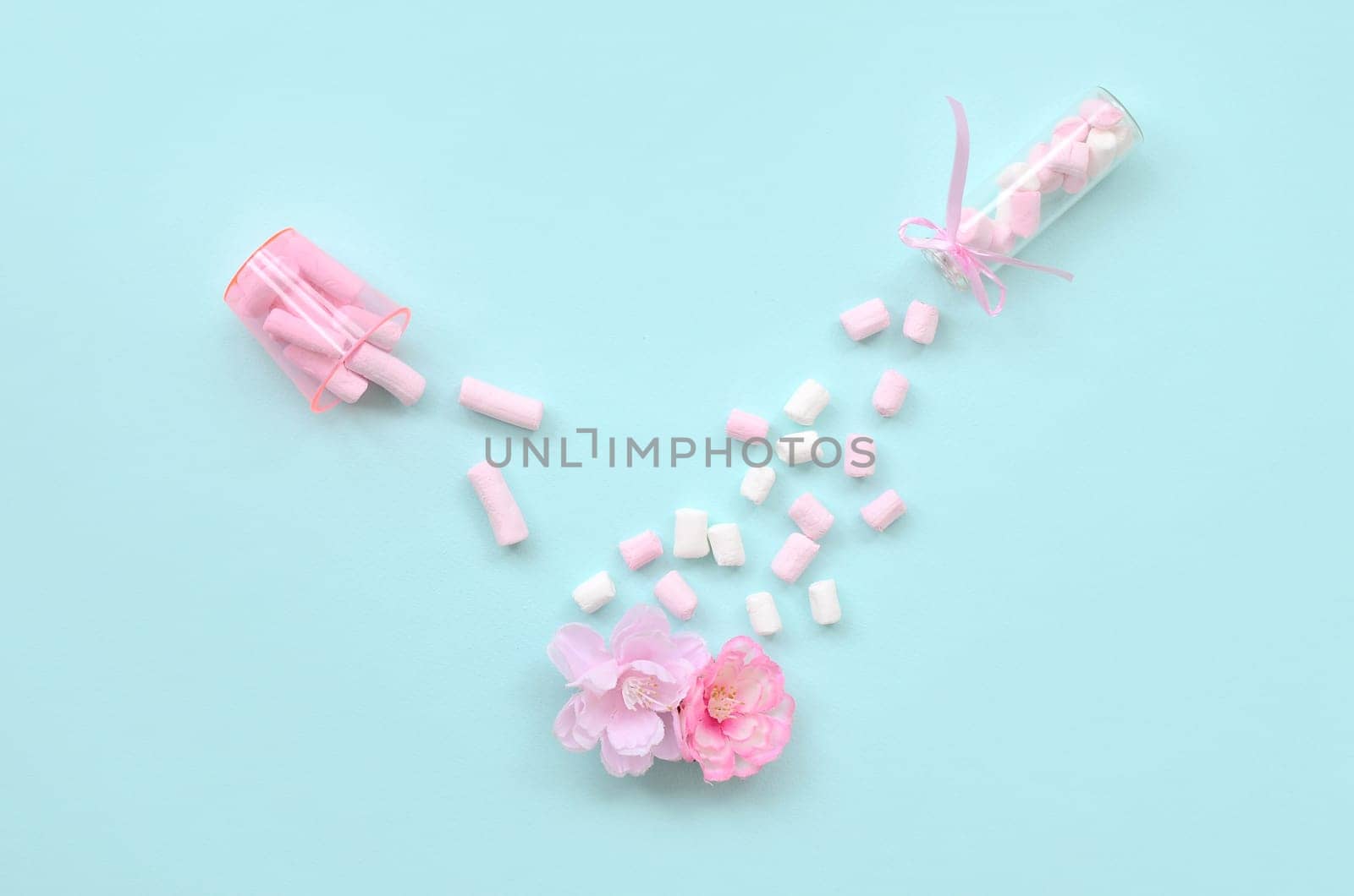 Metaphorical concept of care for flowers. Pink flower sprayed with marshmallows from small transparent tanks on a pastel blue background. Minimal flat lay composition. Top view