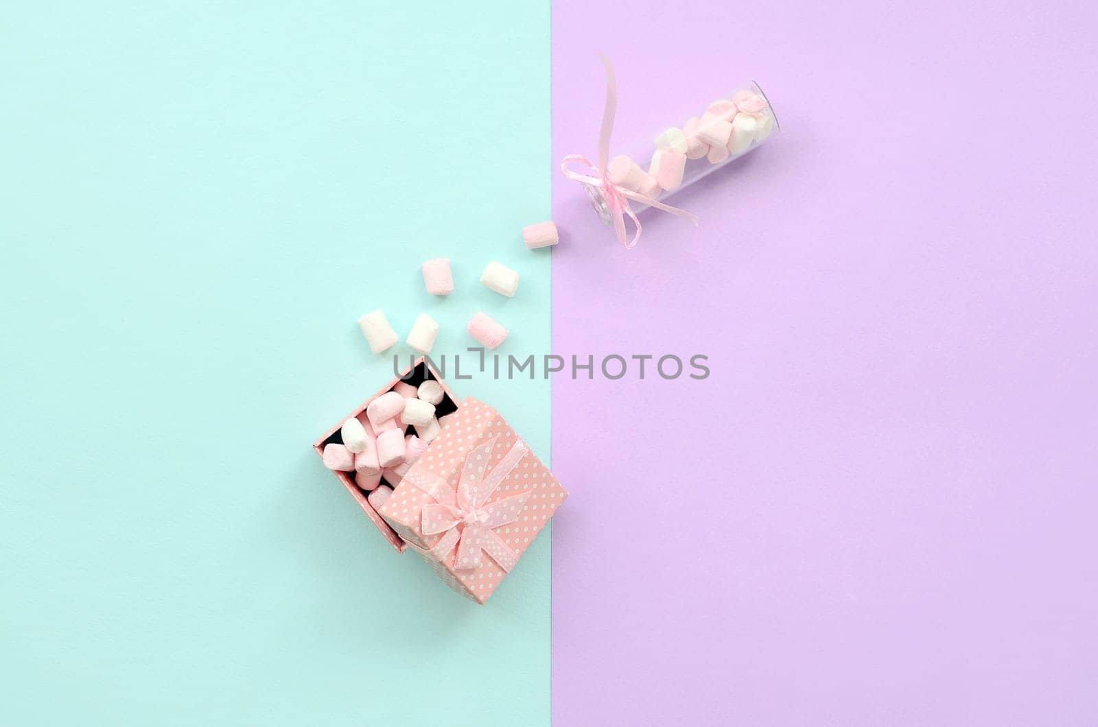 A marshmallow from a glass jar fills a pink gift box on a colored pastel blue and violet background. Minimalism flat lay. Top view