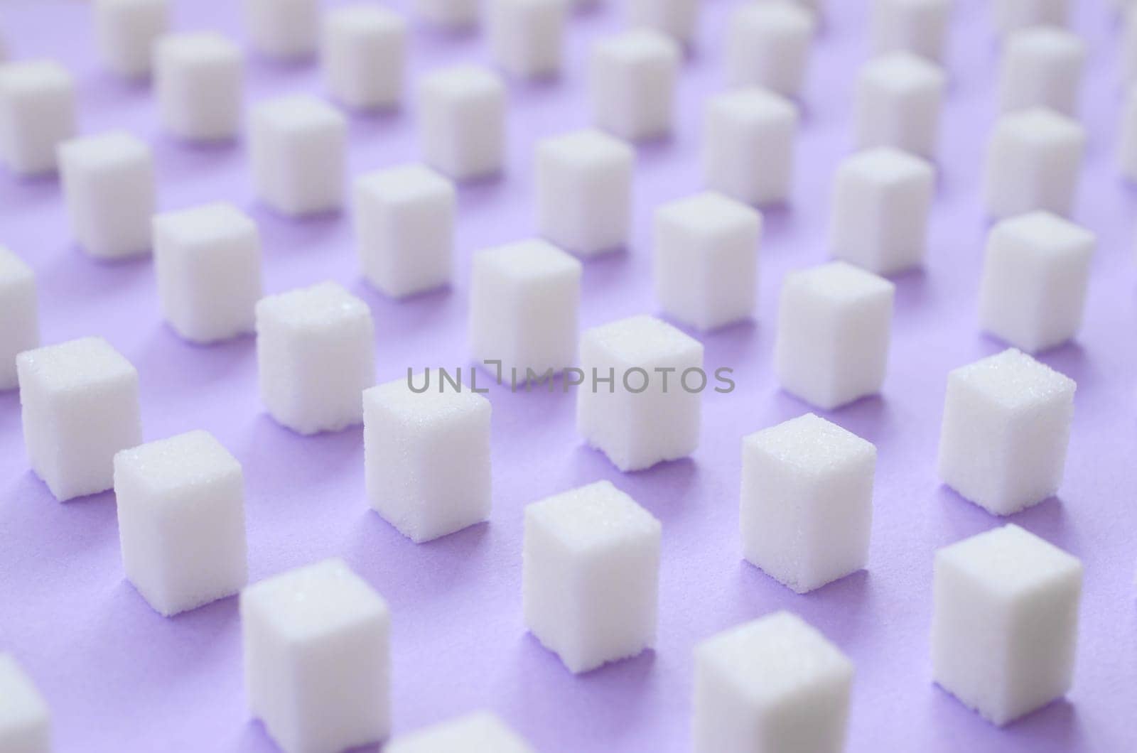 Many small sugar cubes are lined up on a violet background. The concept of diabetes and excess blood sugar