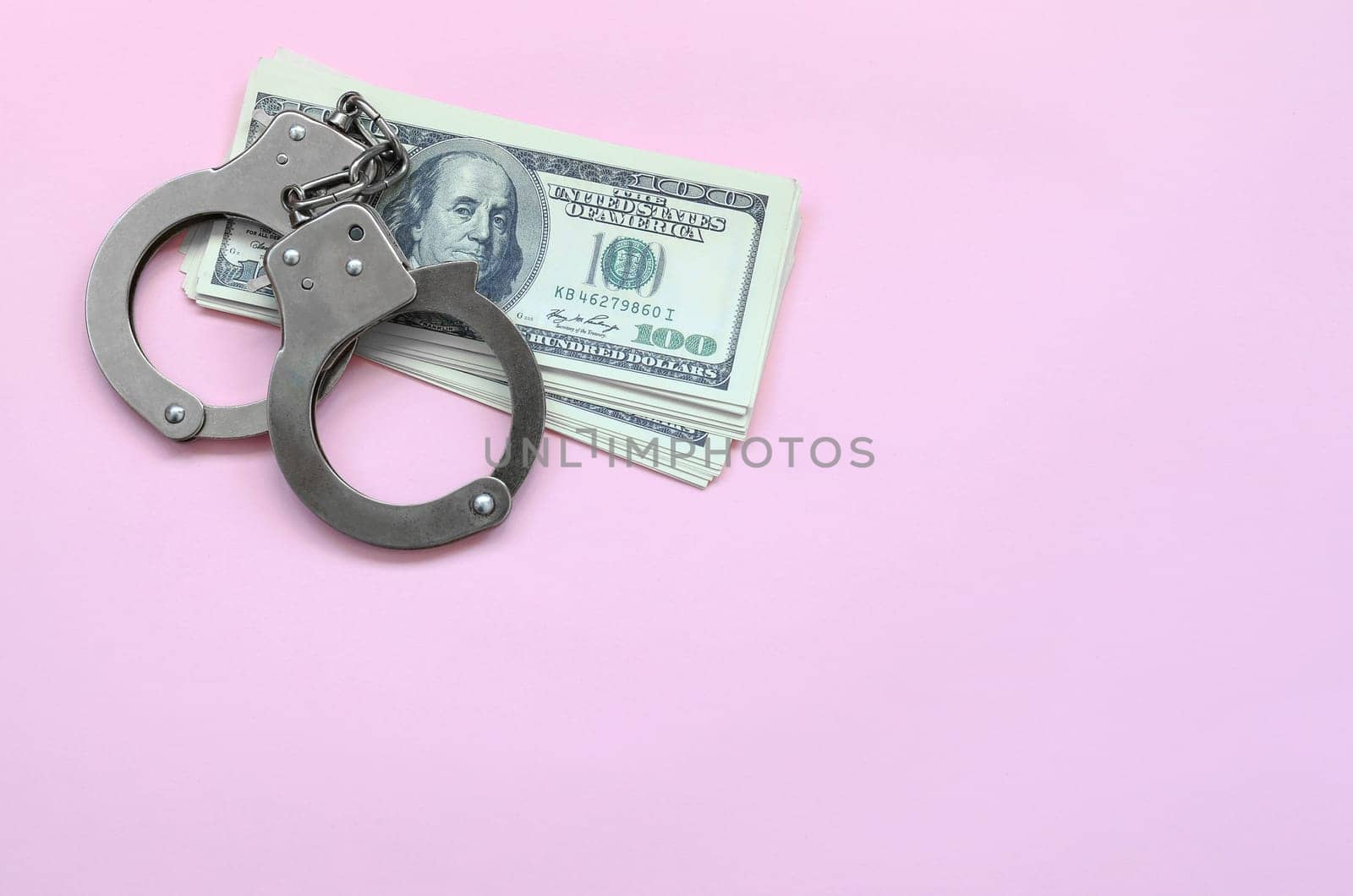 Police handcuffs and hundreds of us dollars lie on a background of living coral color. The concept of punishment for breaking the law in financial transactions