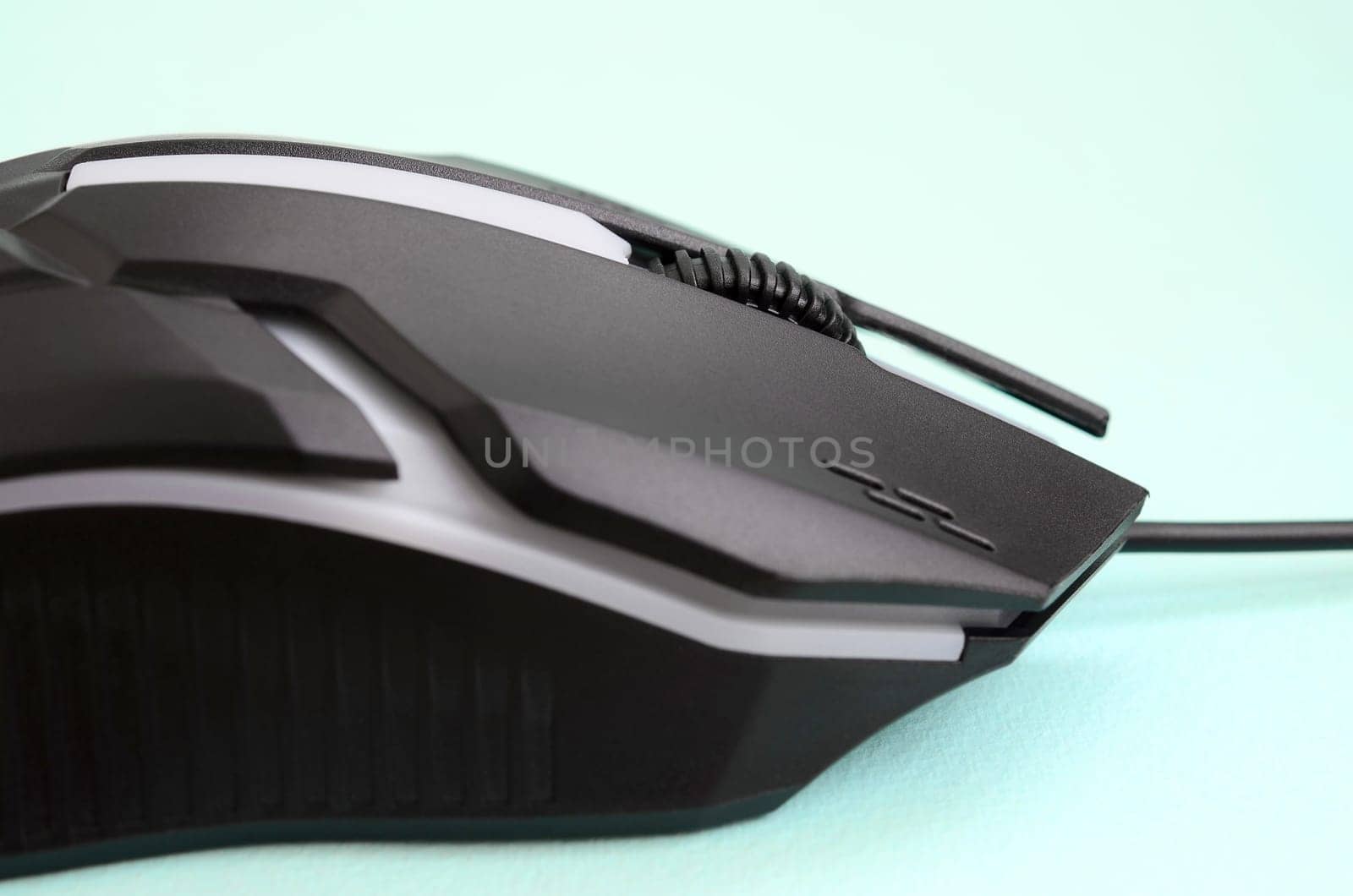 Closeup of a black gaming optical mouse on a blue background. Device for cybersport and online video games