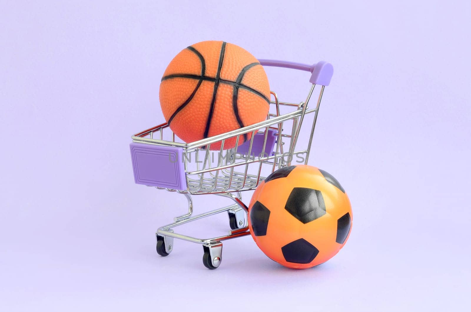 Orange basketball and soccer ball in shopping cart on violet. The concept of selling sports equipment, predictions for sports matches, sports betting