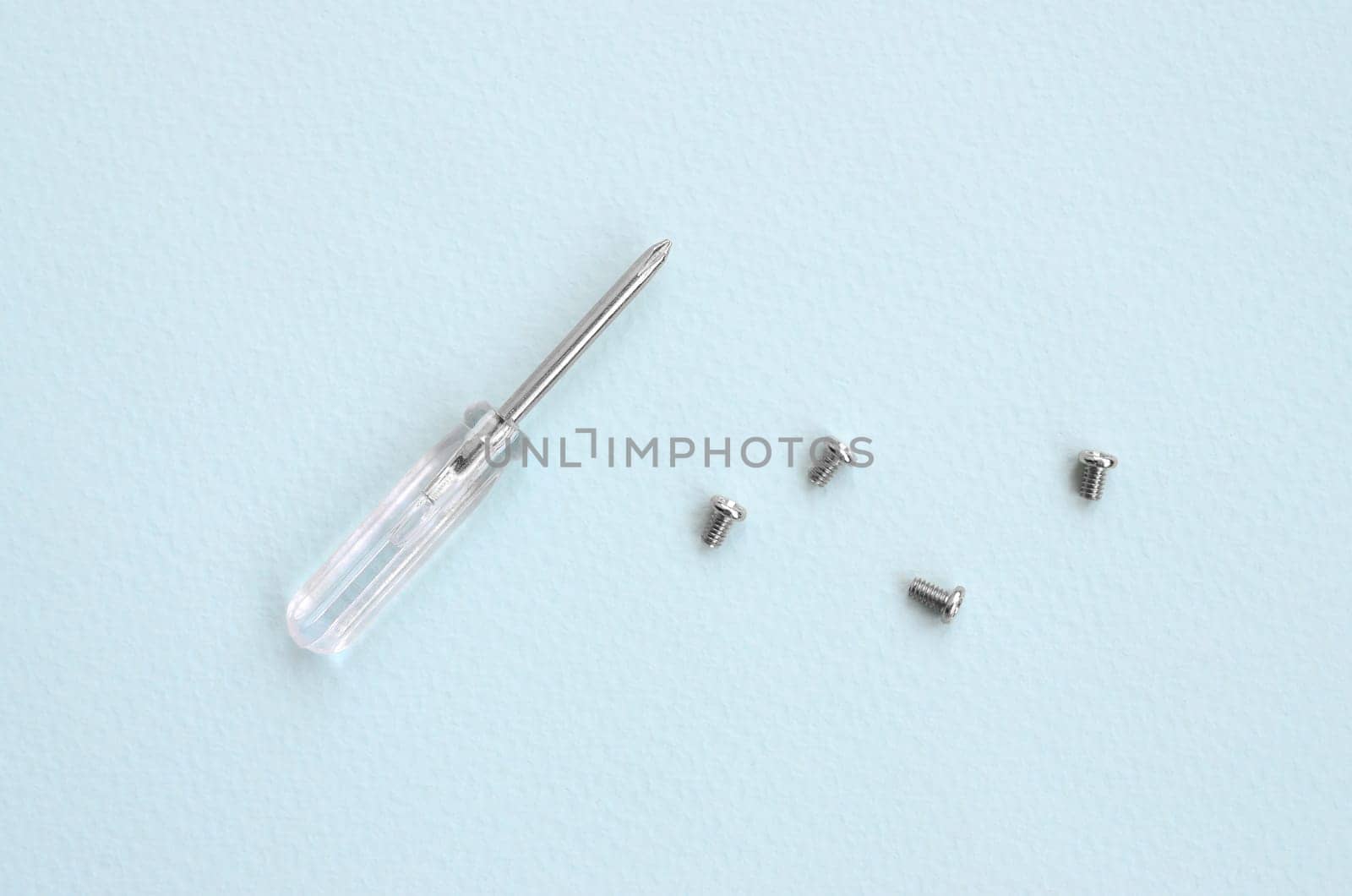 A small screwdriver and a few screws on a blue background. Tools for the repair and disassembly of modern smartphones and mobile devices