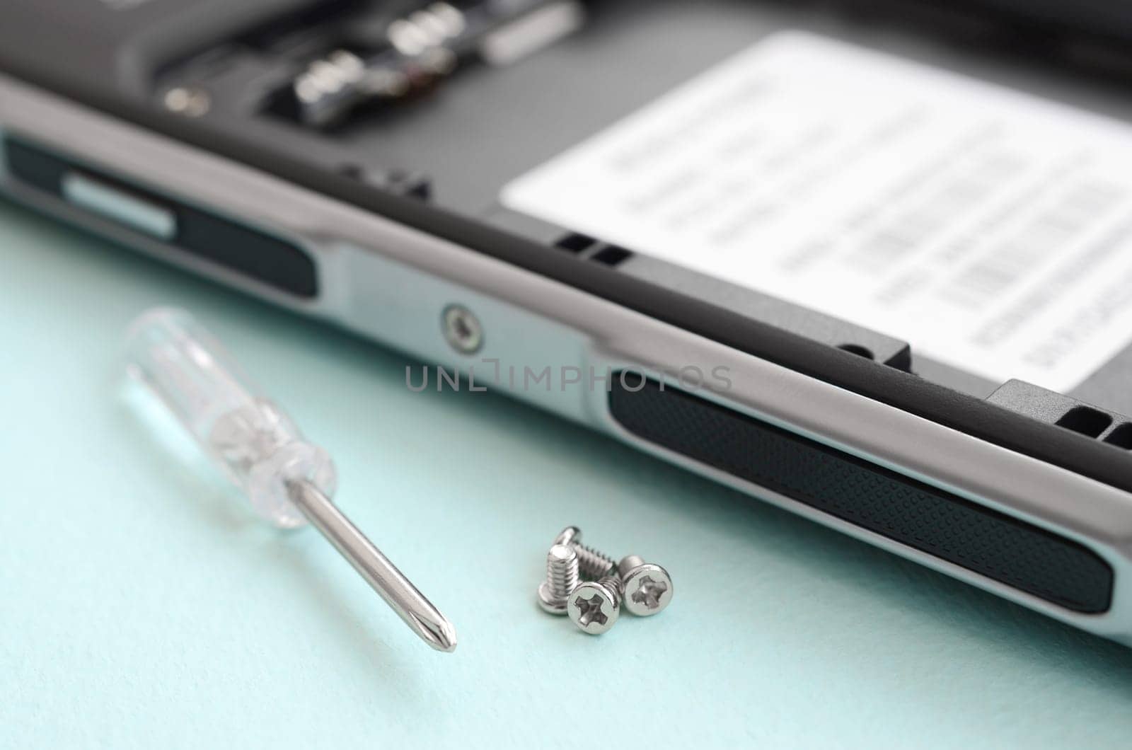 A small screwdriver and a few screws on a blue background. Tools for the repair and disassembly of modern smartphones and mobile devices