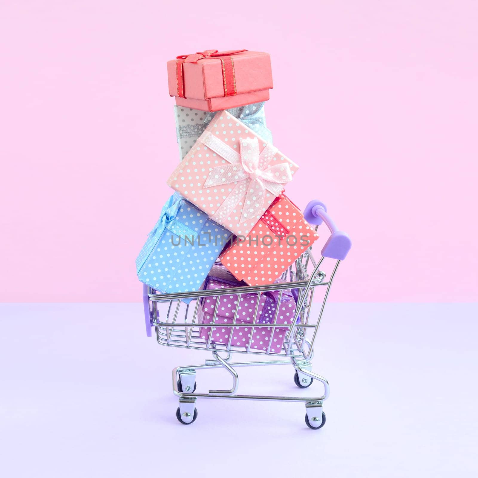 Many colorful present boxes in supermarket shopping cart on violet background. Gifts for winter holidays