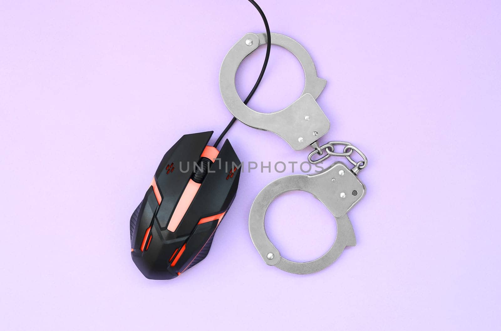 Computer mouse in a red color is chained in handcuffs on the background of purple color. The concept of combating computer crime, hackers and piracy. Flat lay top view