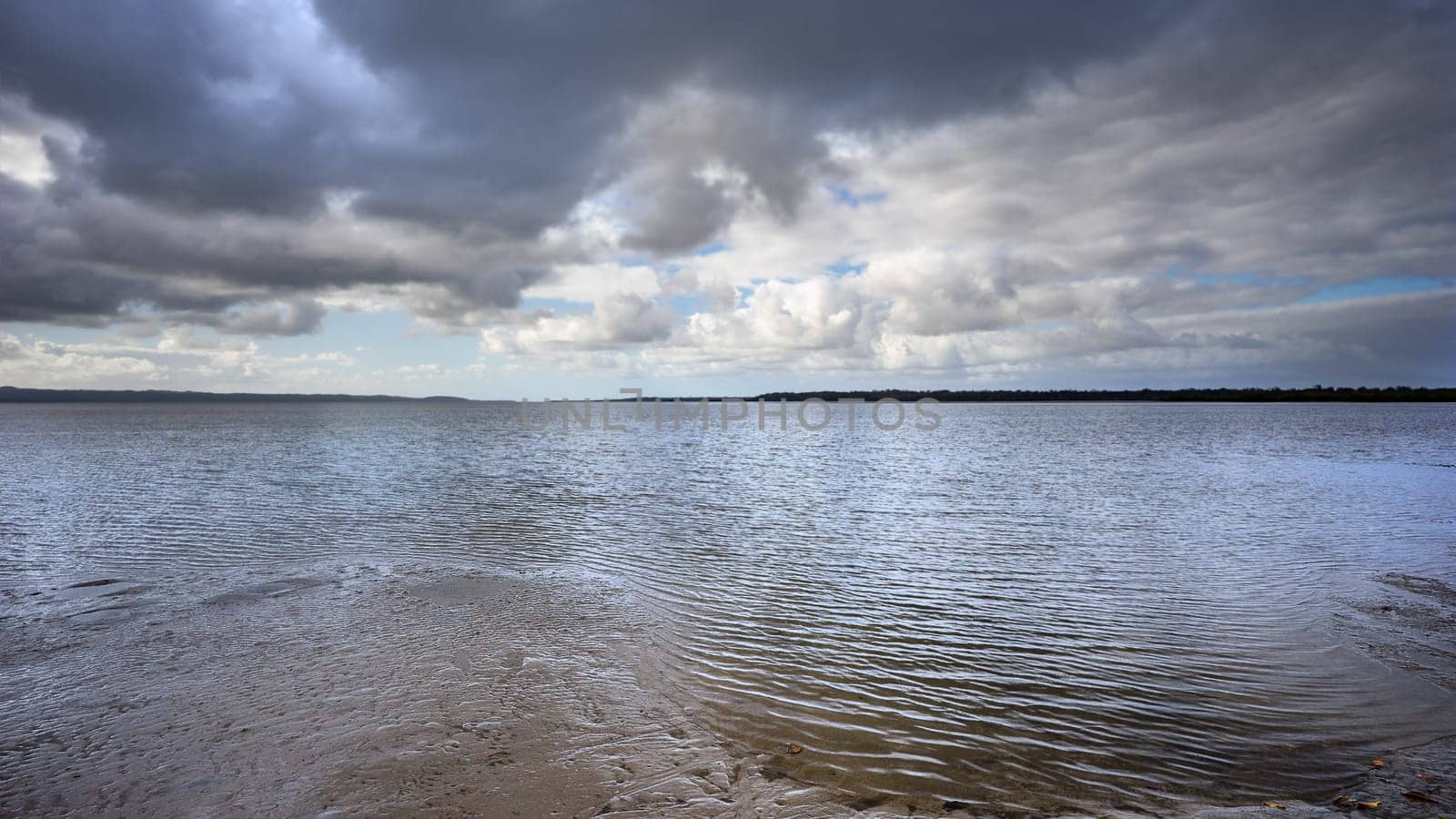 Dramatic storm clouds brewing over the sea and beach at Poona Beach, Queensland. Panorama looking across the Great Sandy Strait, along the Fraser Coast towards the horizon at Inskip Point, Rainbow Beach.