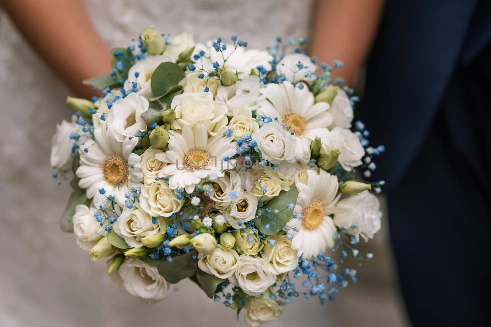 beautiful wedding bouquet in the hands of the bride on the background of a white dress
