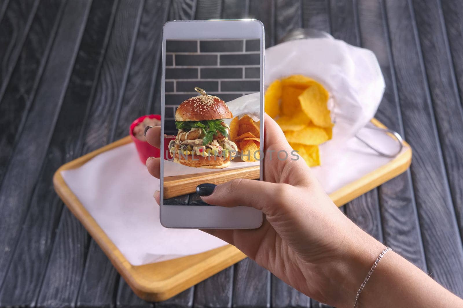 Making photo with phone of bacon burger with nachos on wooden plate. Food blogging.