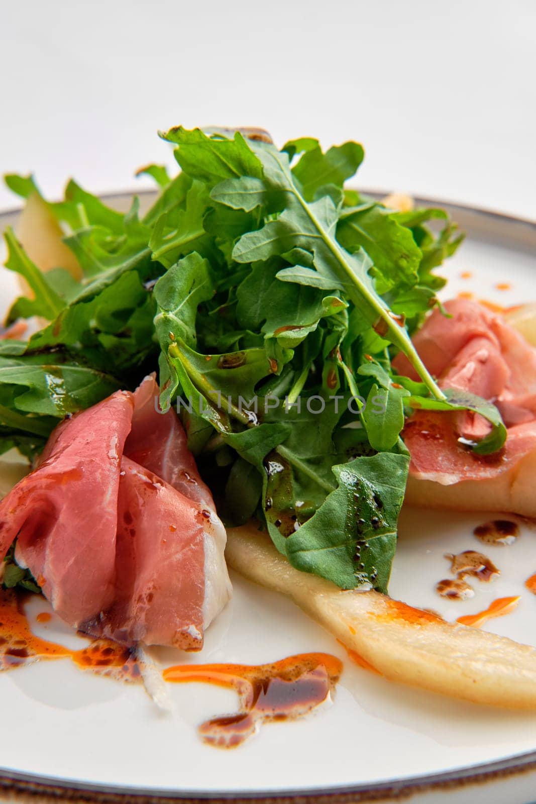 Close up view of salad with jamon, pear and arugula isolated on white