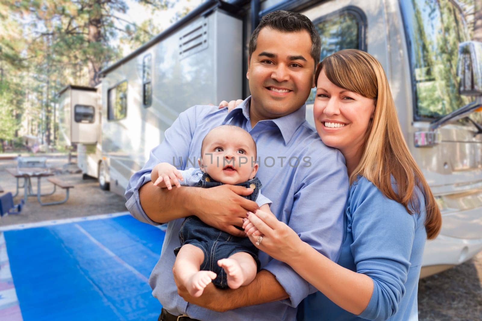 Happy Multiethnic Caucasian and Hispanic Couple with Baby In Front of Their Beautiful RV At The Campground.