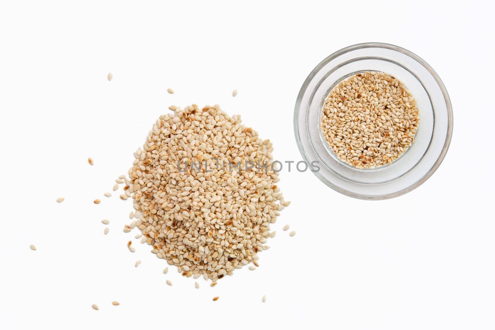 Top view of sesame seeds in a little dish and spilled on white background