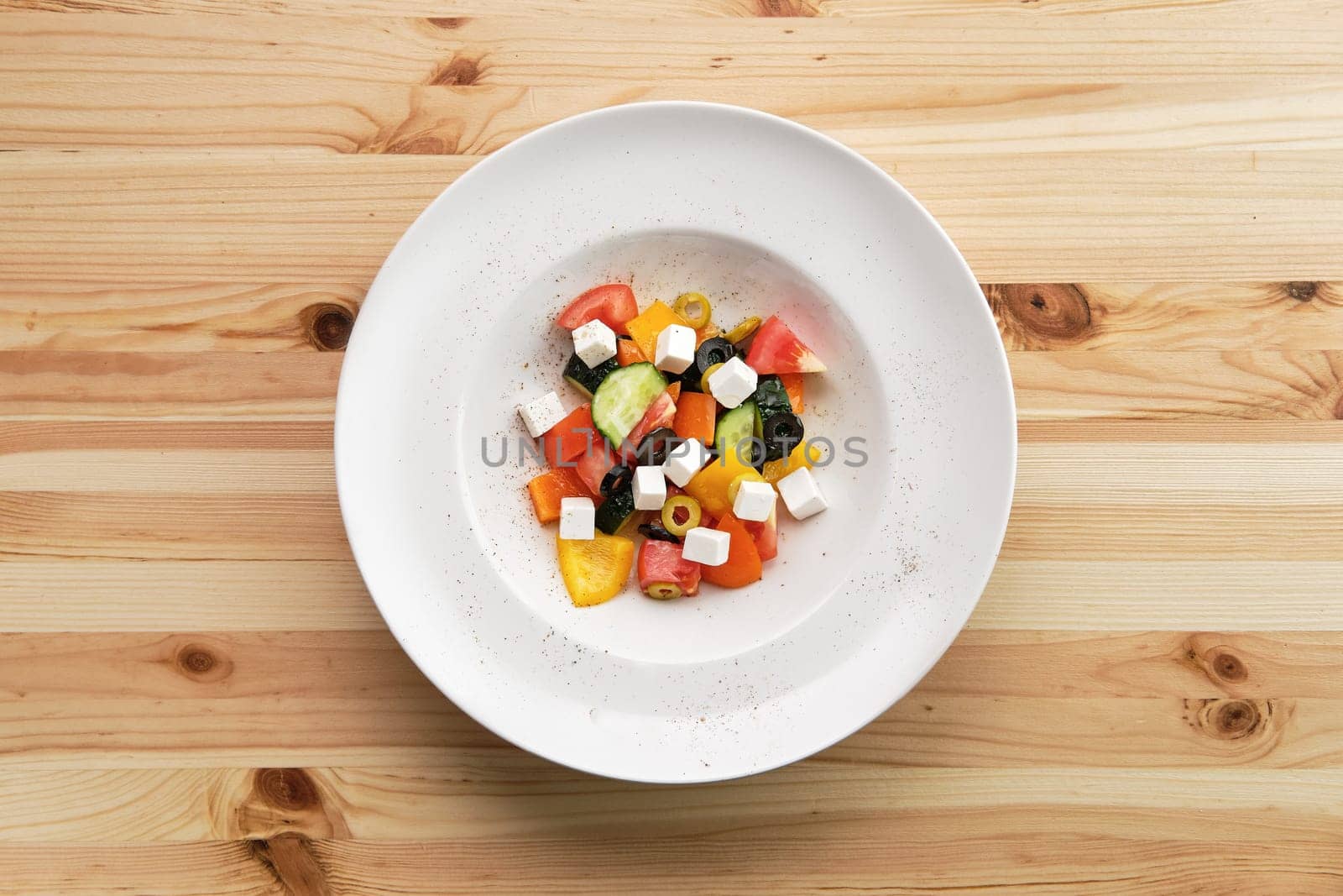 Salad with pepper, tomato, cucumber, olives and feta on wooden table