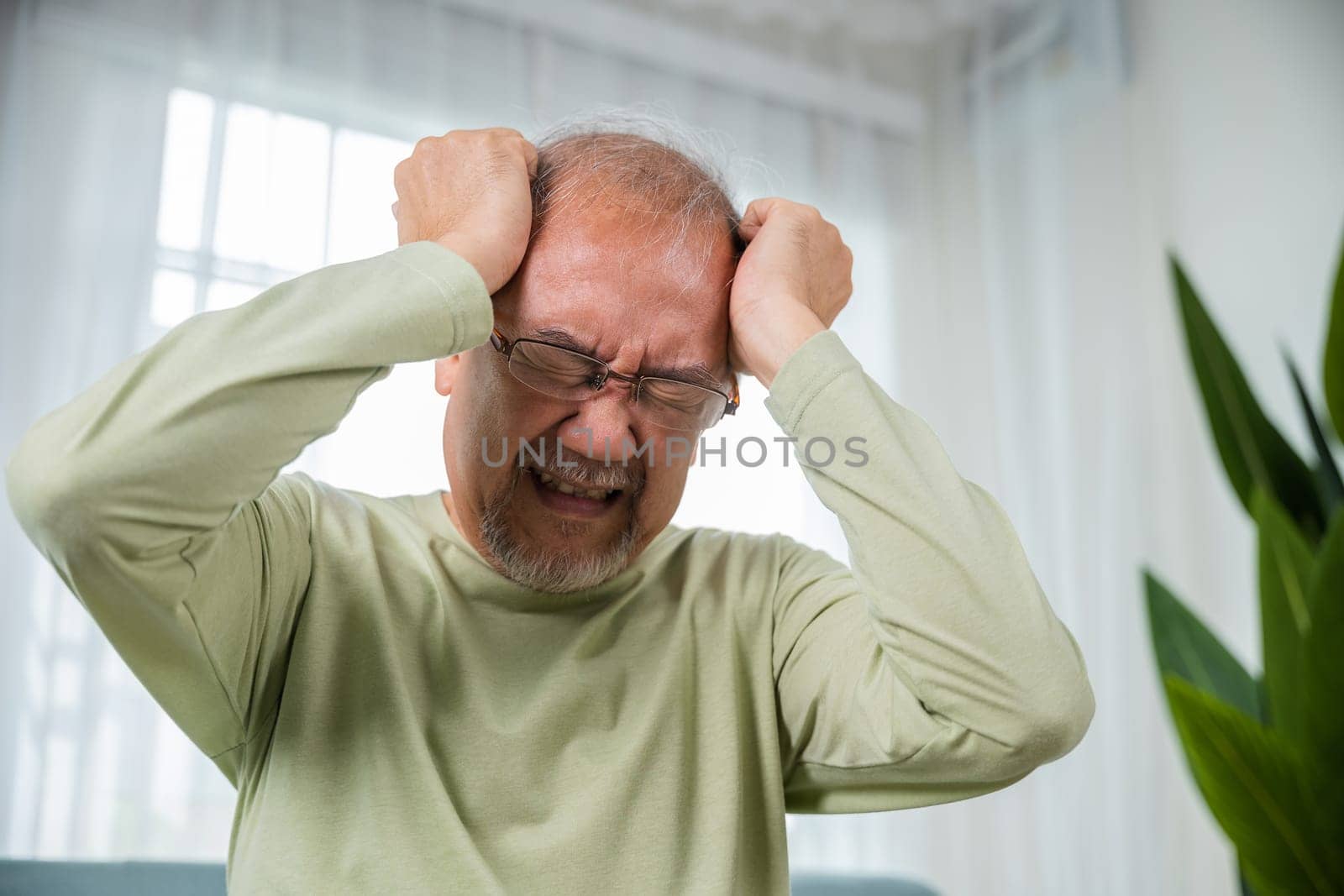 Headache. Close up of elderly holds head with hand suffering from migraine headache, Sad Asian senior man sitting on sofa feeling hurt and lonely at home, Old age health problems, healthcare