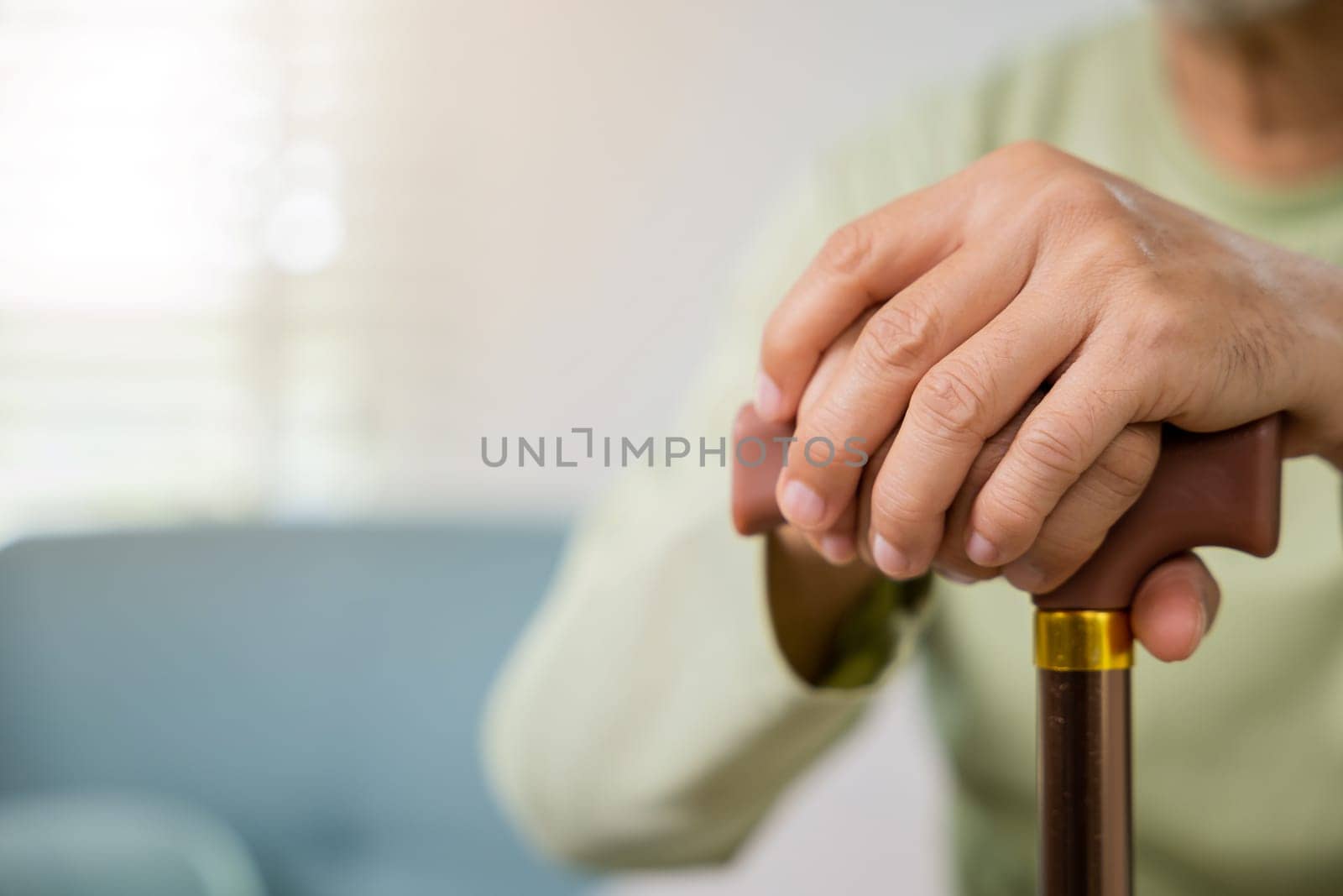 Closeup hands of senior disabled man holding walking stick, Old man sitting resting on sofa hold wooden walking cane, Elderly hand holding handle of cane, International Day for the Elderly