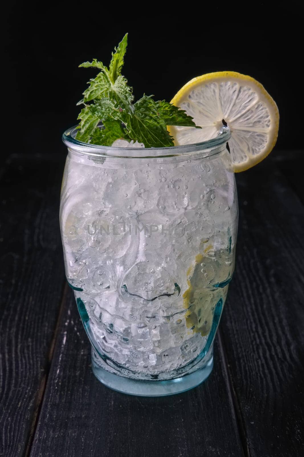 Cold cocktail with vodka and tonic in skull cup on dark wooden background