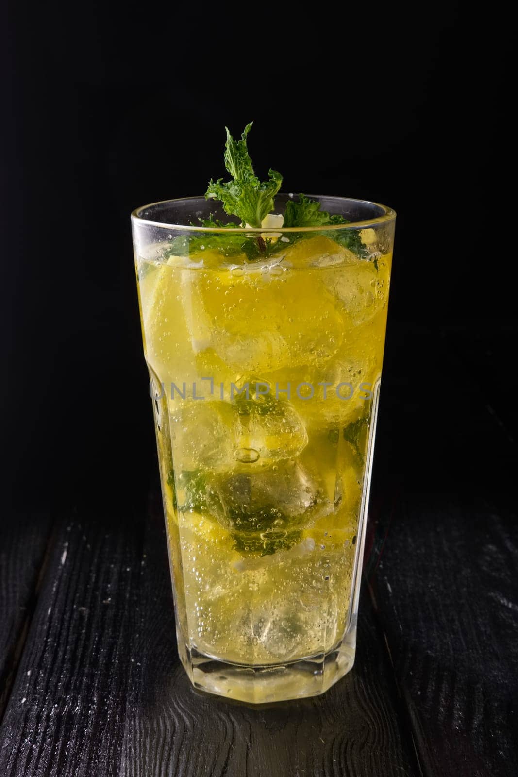 Faceted glass with cold citrus lemonade on dark wooden background
