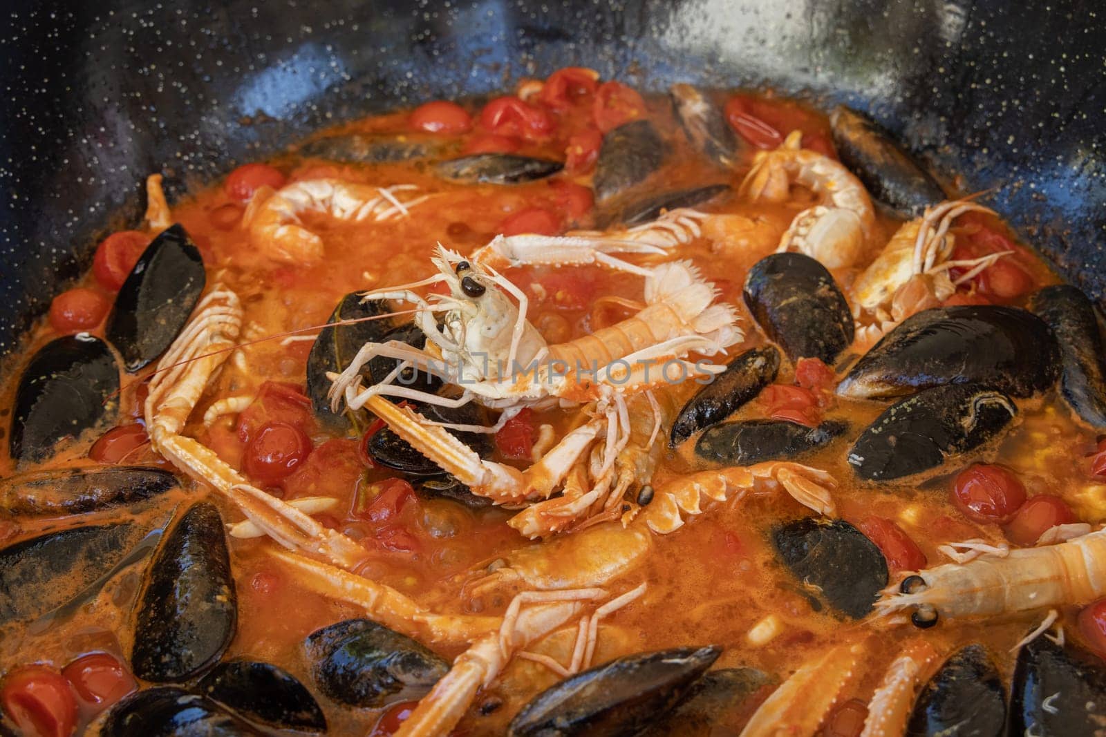 Cooking Italian stew with seafood and tomatoes in a big frying pan. Mediterranean Apulian traditional food with fresh stewed clams, shrimps, mussels, octopus and squid