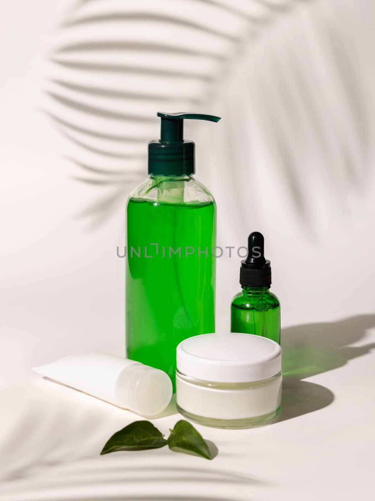 Refillable Cosmetic bottles, jar and tube with green liquid on white, Palm leaf hard shadows, close up, mockup. Skincare beauty products. Natural cosmetics with aloe vera..