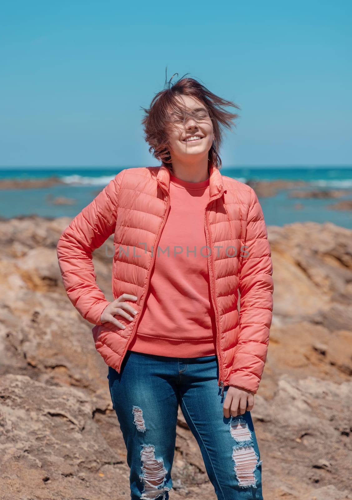 Happy Teen girl wearing pink shirt and pudded jucket, mockup. Teenager standing outdoor near the sea in a sunny day, spending her time alone. Adolescence concept