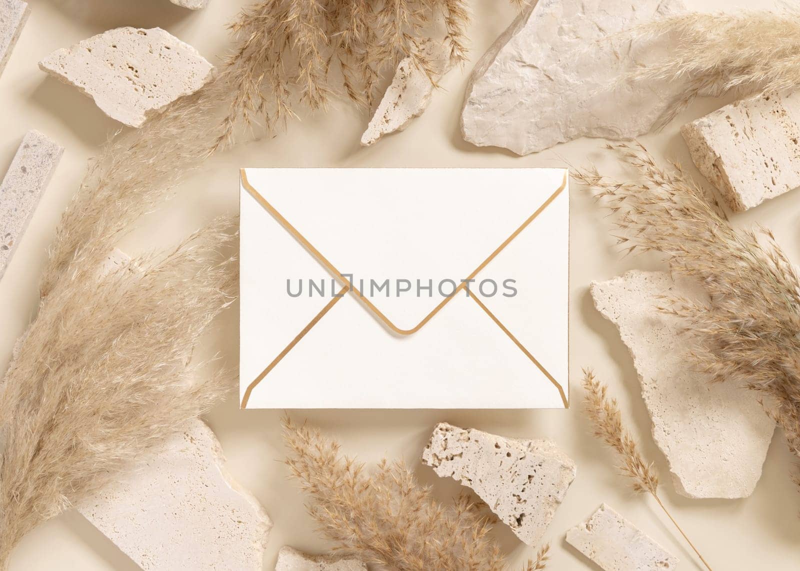 Blank horizontal envelope near beige travertine stones and boho dried pampas grass top view, mockup. Bohemian greeting or wedding Invitation. Close to nature.