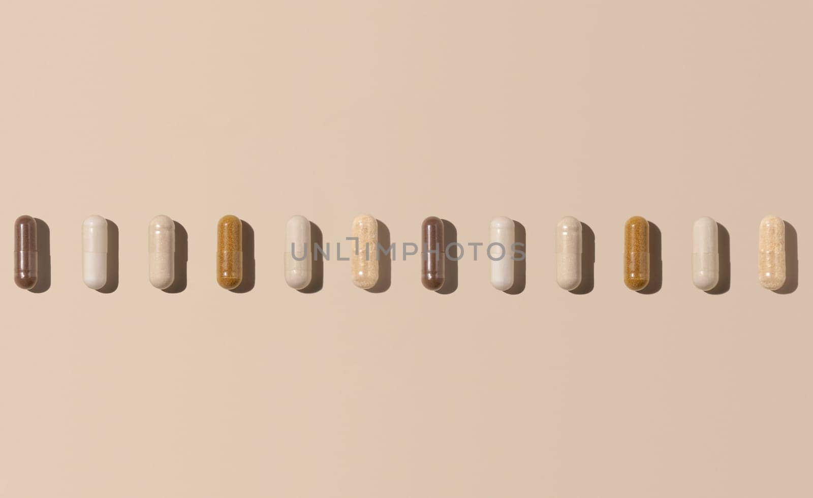 Mix of medical capsules in a line on light beige top view, hard shadows. Preventive medicine and healthcare, dietary supplements and vitamins. Assorted pharmaceutical medicine capsules