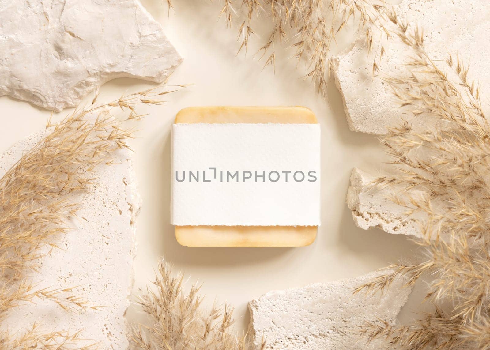 Soap bar with blank label near beige travertine stones and dried pampas grass top view, mockup. Boho scene handmade soap. Bohemian or close to nature .