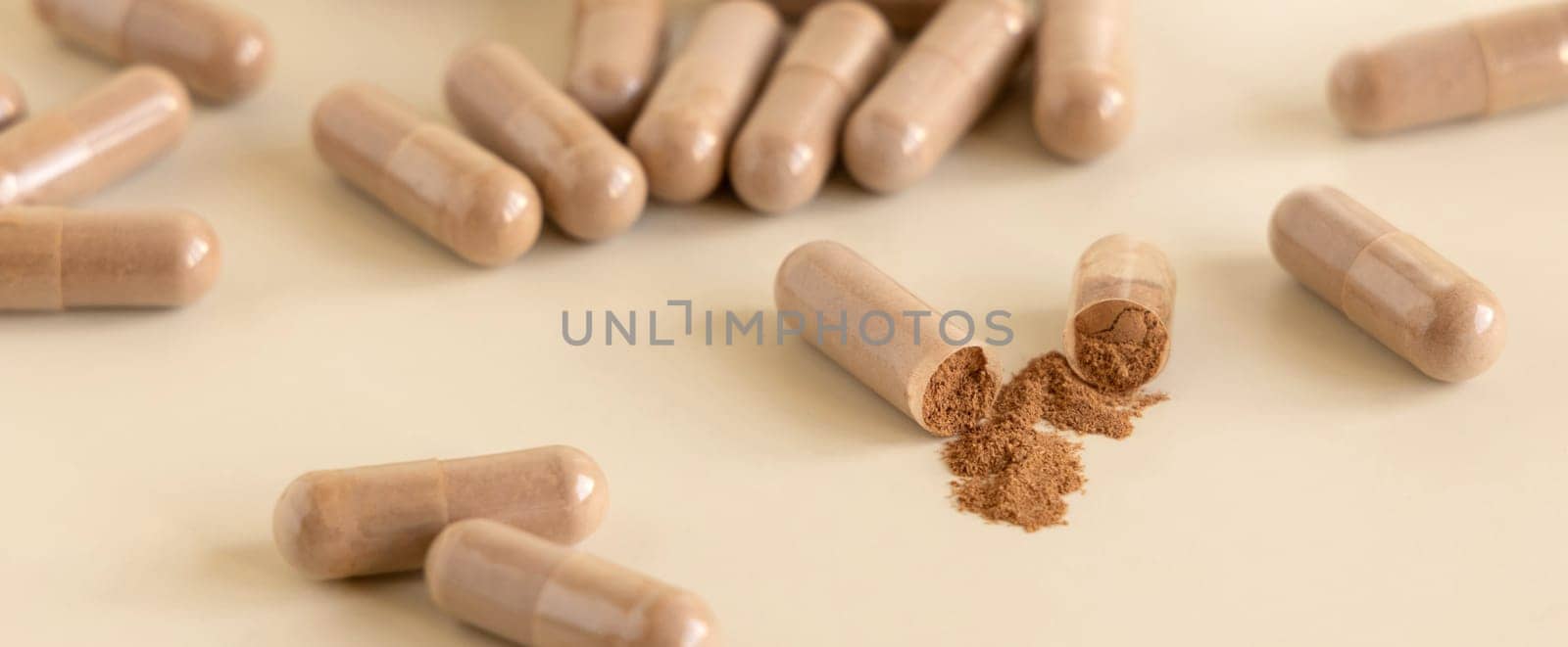 Medical capsules on light beige close up. One capsule opened to show brown powder. Preventive medicine and healthcare, taking dietary supplements and vitamins. Pharmaceutical product