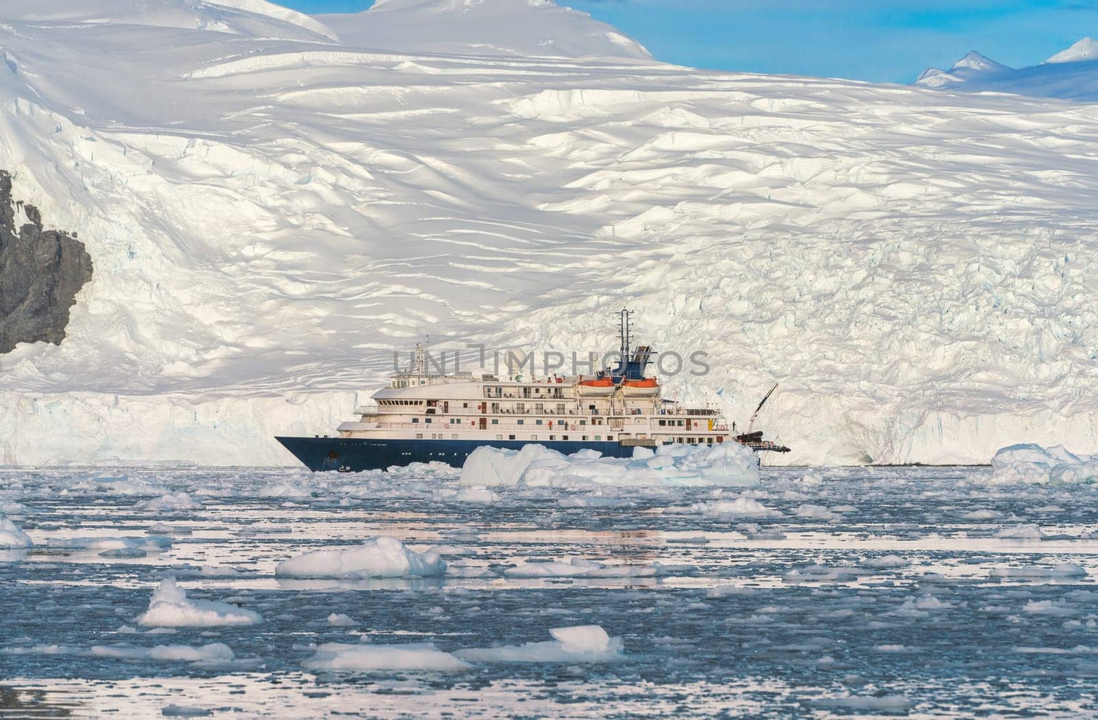 a Blue expedition ship in front of Antarctic iceberg landscape in Cierva Cove - a deep inlet on the west side of the Antarctic Peninsula, surrounded by dramatic glacier fronts