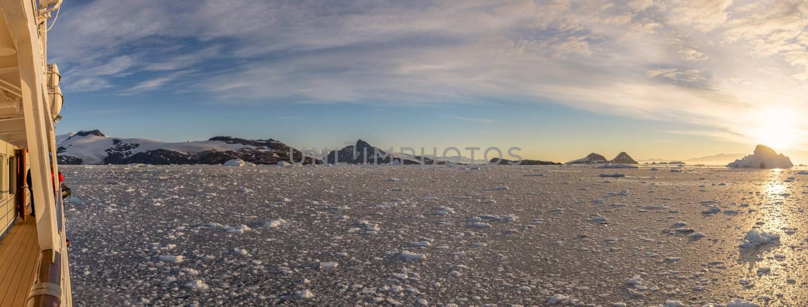 Cruise ship sails through wintry Cierva Cove - a deep inlet on the west side of the Antarctic Peninsula, ringed by Cierva Bay in San Martín Land - Antarctica, during a dramatic sunset